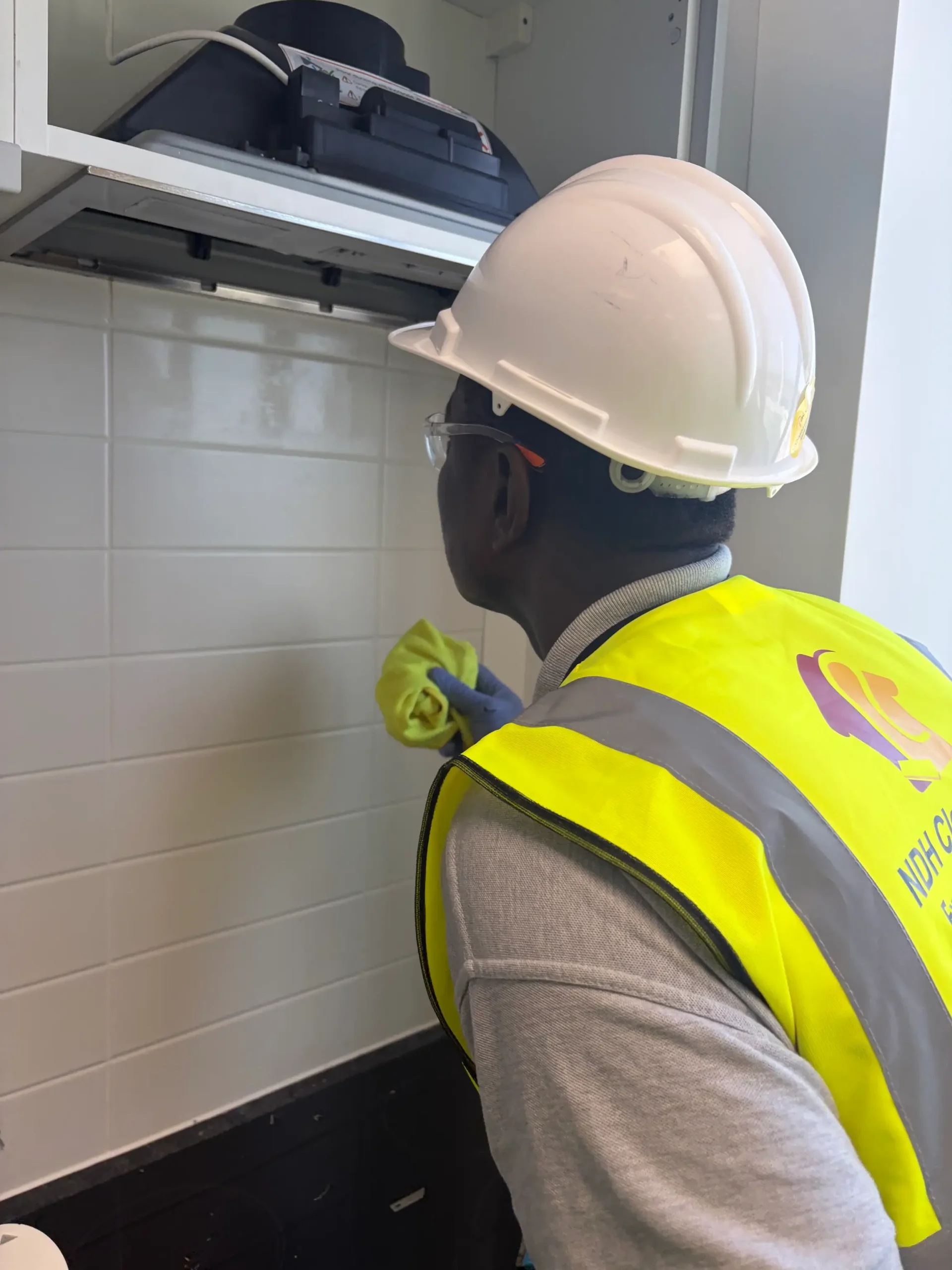 NDH Cleaning Operative wearing a hard hat, hi-vis and safety glasses cleaning a oven fan
