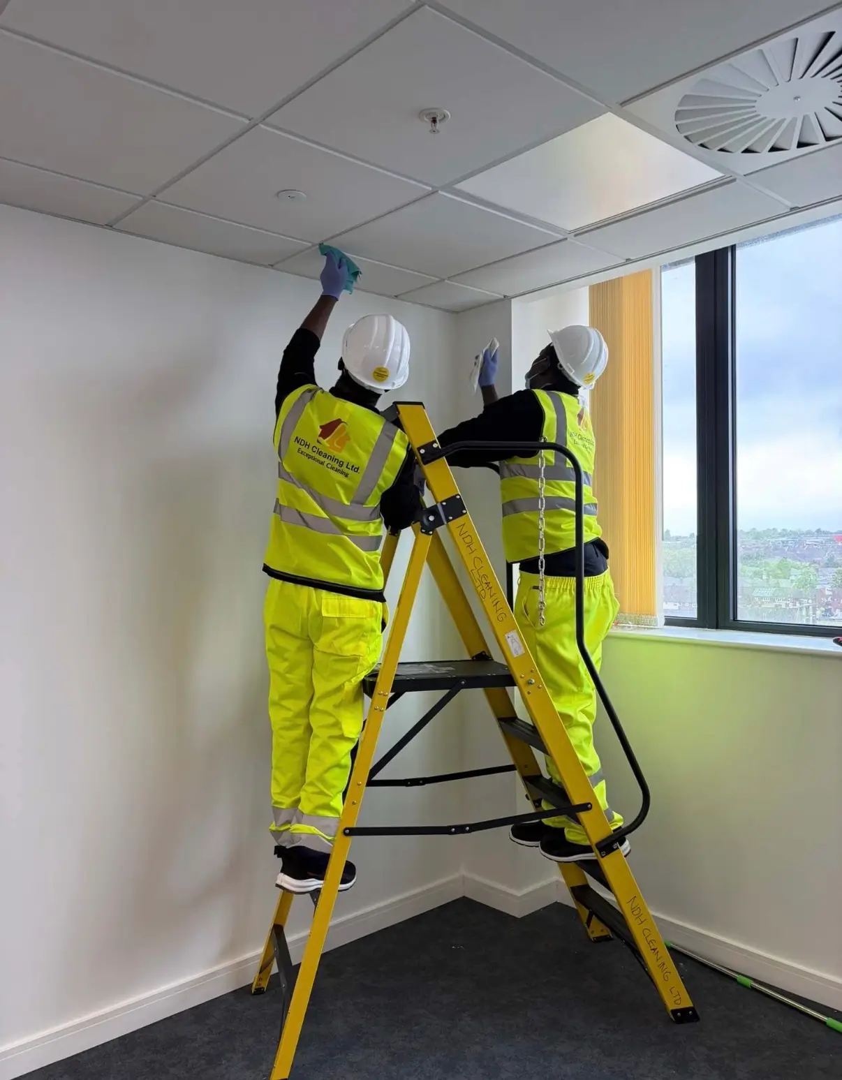 Two NDH Cleaning Ltd operatives working from step ladders to clean ceilings and walls in an office before handover
