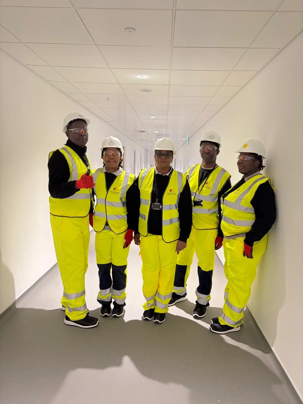 Team of five NDH Cleaning Ltd operatives in yellow hi-vis coveralls, hard hats and safety glasses in a newly built corridor