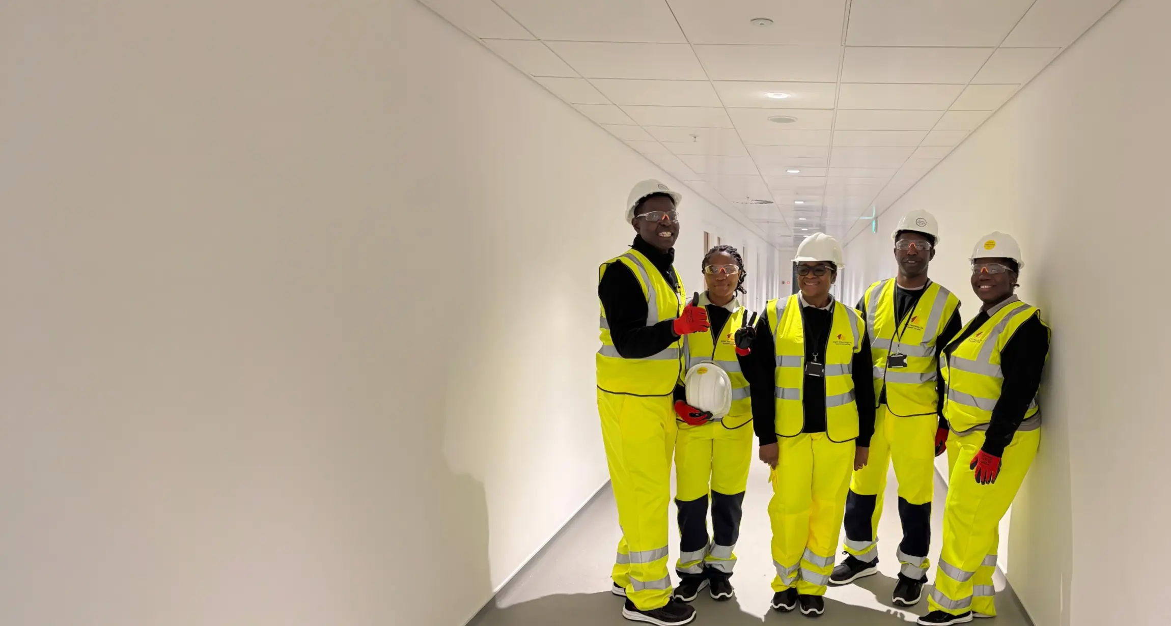 Team of five NDH Cleaning Ltd operatives in yellow hi-vis coveralls, hard hats and safety glasses in a newly built corridor